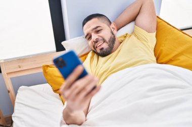 Young latin man using smartphone lying on bed at bedroom