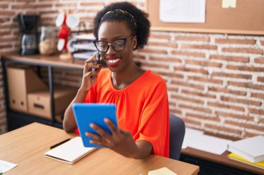 African american woman business worker talking on smartphone using touchpad at office