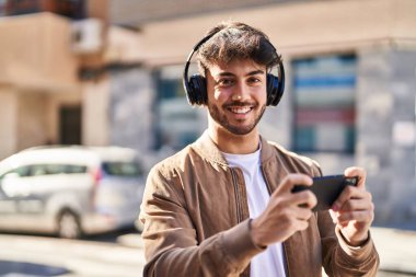 Young hispanic man smiling confident playing video game at street