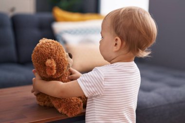 Sevimli çocuk evde oyuncak ayıyla oynuyor.