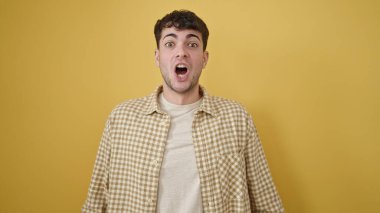 İzole edilmiş sarı arka planda sürpriz bir ifadeyle duran İspanyol genç adam.