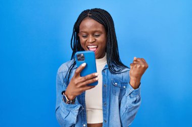 Örgülü Afrikalı kadın akıllı telefon kullanarak mesaj yazıyor. Gururla bağırıyor, zaferi kutluyor ve kollarını kaldırarak başarıyı kutluyor. 