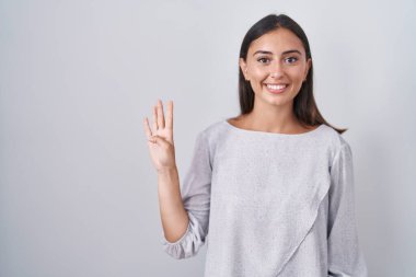 Young hispanic woman standing over white background showing and pointing up with fingers number four while smiling confident and happy. 