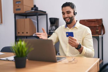 Çağrı merkezi kulaklığı takan İspanyol genç adam online alışveriş yapıyor başarıyı mutlu bir gülümsemeyle kutluyor ve kazanan el kaldırarak ifade ediyor 