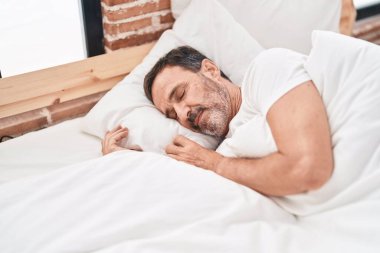 Orta yaşlı bir adam yatakta uzanıyor, yatak odasında uyuyor.