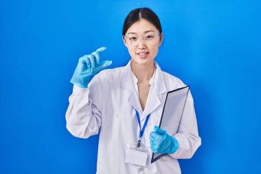 Bilimadamı laboratuvarında çalışan Çinli genç bir kadın gülümsüyor ve el hareketleriyle hareket ediyor parmaklarıyla işaret yapıyor ve kameraya bakıyor. ölçüm kavramı. 