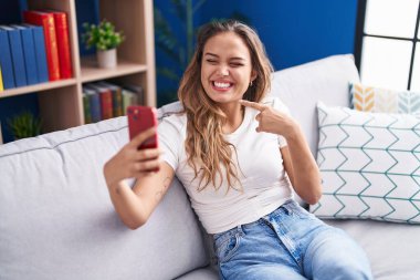 Genç İspanyol kadın akıllı telefonuyla video görüşmesi yapıyor. Gülümsüyor. Elinle ve parmağınla mutlu işaret ediyor. 