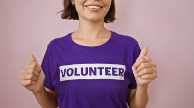 Hevesli genç İspanyol kadın gönüllü, kendine güveni tam, kısa saçlı ve hayırsever üniformalı, pembe bir arka planda sırıtan,