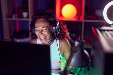 Middle age woman streamer playing video game using computer at gaming room