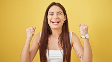 Genç, güzel, İspanyol bir kadın gülümsüyor. Kazanan yüz ifadesiyle izole edilmiş sarı arka planda duruyor.