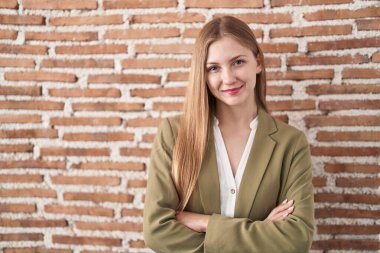 Duvarın arkasında duran beyaz bir kadın kollarını kavuşturup kameraya bakarken gülümsüyor. pozitif kişi. 
