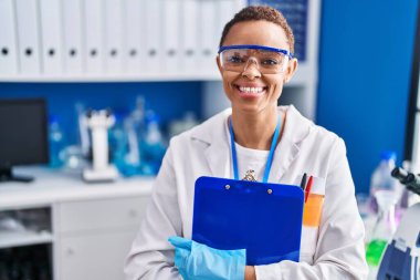 Afrikalı Amerikalı bilim kadını gülümsüyor. Laboratuvarda elinde bir pano var.