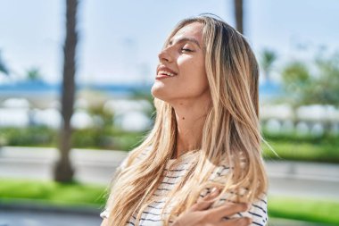 Parkta gözleri kapalı nefes alan genç sarışın kadın.