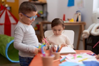 Anaokulunda masa başında oturmuş kağıt kesen sevimli bir kız ve çocuk.