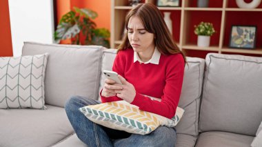 Evdeki kanepede oturan, akıllı telefon kullanan genç İspanyol kadın.