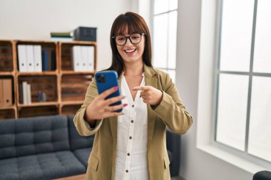 Ofiste çalışan genç esmer kadın akıllı telefonuyla gülümsüyor. 