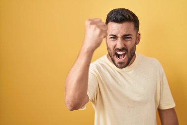 Sarı arka planda dikilen yakışıklı İspanyol sinirli ve kızgın yumruğunu kaldırırken sinirli ve öfkeliydi. öfke ve agresif konsept. 