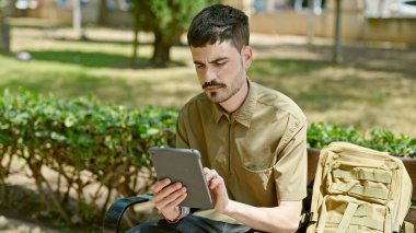 Parktaki bankta oturan dokunmatik ped kullanan genç İspanyol turist.
