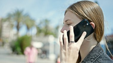 Sokakta ciddi bir ifadeyle akıllı telefondan konuşan genç sarışın kadın.