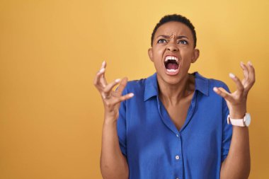 Sarı arka planda duran Afrikalı Amerikalı kadın çılgın ve kızgın bir şekilde bağırıyor ve agresif bir ifade ve kollarla bağırıyor. hüsran kavramı. 