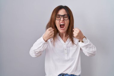 Esmer kadın öfkeli ve öfkeli bir şekilde arka planda duruyor öfkeyle bağırırken yumruklarını kaldırıyor. öfke ve agresif konsept. 