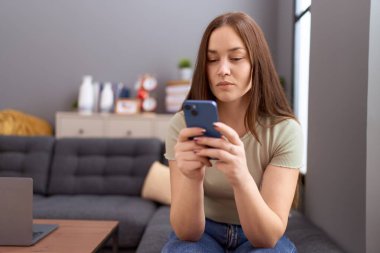 Genç ve güzel bir kadın evde akıllı telefon kullanıyor.