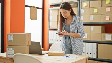 Genç ve güzel İspanyol kadın ecommerce işçisi ofiste fotoğraf paket yapıyor.