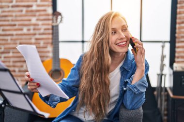 Genç sarışın müzisyen, müzik stüdyosunda kanepede oturmuş akıllı telefondan konuşuyor.