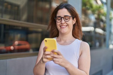 Sokakta akıllı telefon kullanan kendine güvenen genç bir kadın.