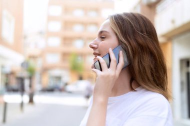 Beyaz bir kadın gülümsüyor ve caddede akıllı telefondan konuşuyor.