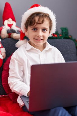 Evdeki yılbaşı dekorasyonunda dizüstü bilgisayar kullanan sevimli İspanyol çocuk.