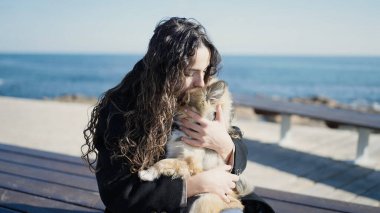 Köpekli genç İspanyol kadın deniz kenarında bankta oturmuş öpüşüyor.