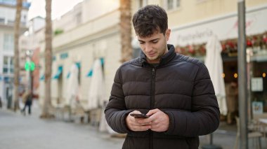 Kahve dükkanının terasında akıllı telefon kullanan genç bir İspanyol.