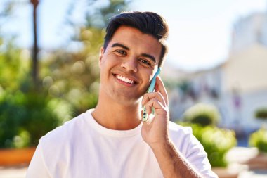 Genç İspanyol adam gülümsüyor. Parktaki akıllı telefondan konuşuyor.