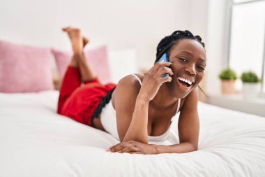 African american woman talking on smartphone lying on bed at bedroom