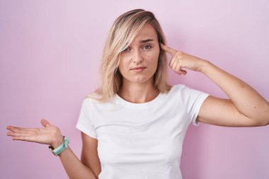 Pembe arka planda duran genç sarışın kadın avucunun içi açık, fotokopi alanı gösteren ve alnını işaret eden avuçlardan rahatsız. Bunu bir düşün.. 