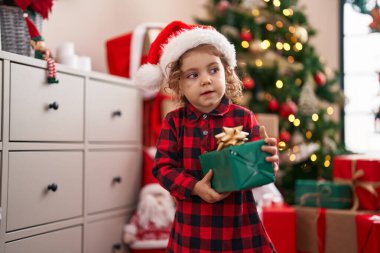 Sevimli beyaz kız elinde hediyeyle Noel ağacının yanında duruyor.