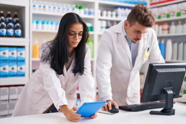 Eczanede çalışan erkek ve kadın eczacılar dokunmatik ped ve bilgisayar kullanıyorlar.
