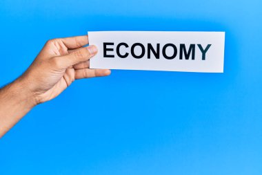 Hand of caucasian man holding paper with economy word over isolated blue background
