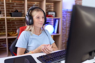 Video oyunları oynayan, kulaklık takan, elleri çapraz parmaklı, gevşemiş ve neşeli gülümseyen beyaz bir kadın. Başarı ve iyimserlik 