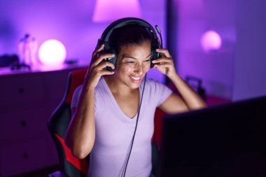 Young beautiful hispanic woman streamer playing video game using computer at gaming room