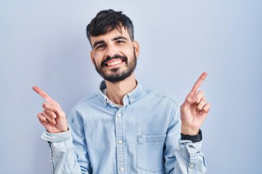 Mavi arka planda duran sakallı, kendine güvenen, farklı yönleri gösteren genç İspanyol bir adam. reklam için kopyalama alanı 
