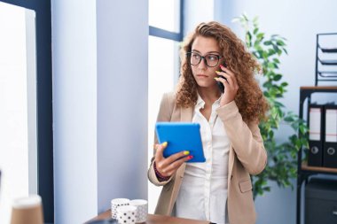 Genç, güzel İspanyol iş kadını dokunmatik ped kullanıyor. Ofiste akıllı telefondan konuşuyor.