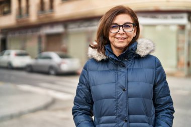 Orta yaşlı kadın sokakta kendine güvenen gözlüklü gülümsüyor.