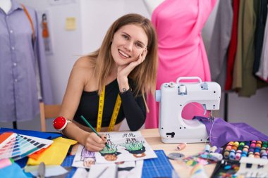 Young blonde woman tailor smiling confident drawing clothing design at tailor shop