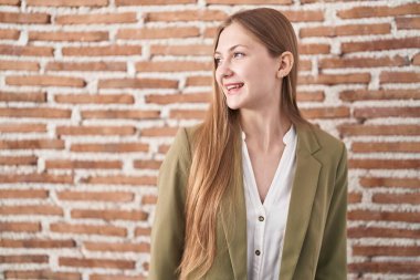 Duvarın arkasında duran beyaz bir kadın yüzünde gülümseme, doğal bir ifade ile bir o yana bir bu yana bakıyor. Kendinden emin gülen. 