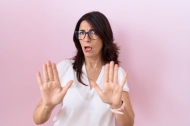 Orta yaşlı İspanyol kadın, günlük beyaz tişört ve gözlük giyip avuç içlerini hareket ettirerek reddediyor ve iğrenç bir ifadeyle reddediyor. Dur ve yasakla. 