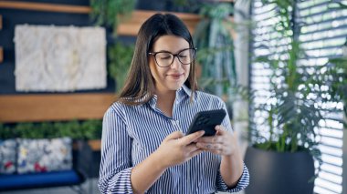 Ofiste akıllı telefon kullanarak mutlu gülümseyen güzel İspanyol kadın.