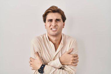 Young man standing over isolated background shaking and freezing for winter cold with sad and shock expression on face 