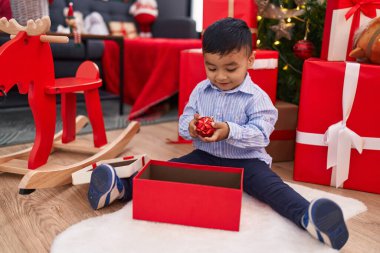 Tapılası İspanyol bebek elinde noel balosu süsü tutarak evde oturuyor.
